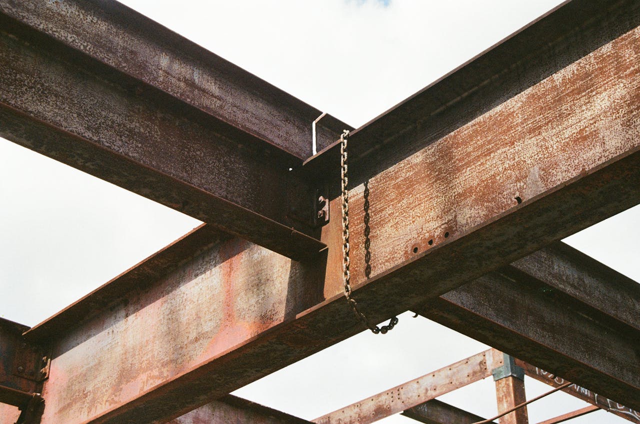 hero-img-01 Close-up of rusty steel beams and chains in outdoor industrial construction site.
